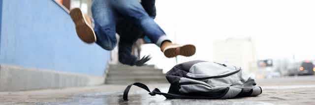 A person stumbles, with a backpack on the ground in the foreground