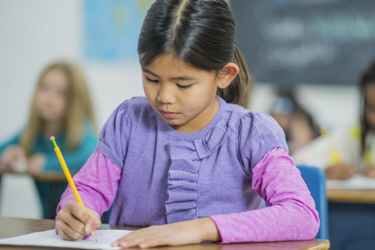 A child sits at a desk marking a paper with a pencil.