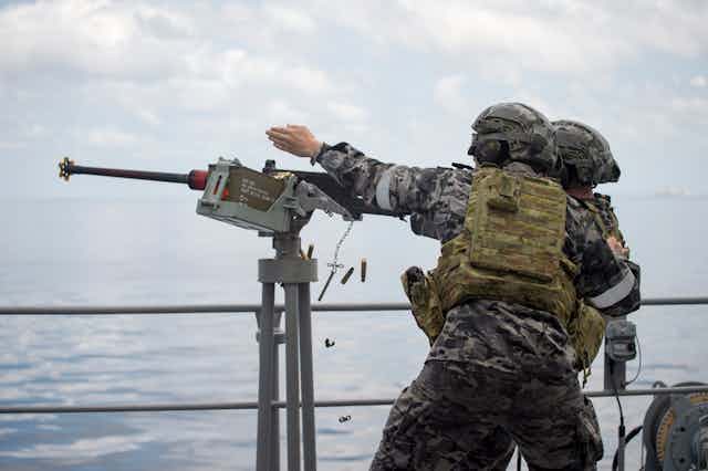 Defence personnel onboard a ship firing a gun in a mock sea battle