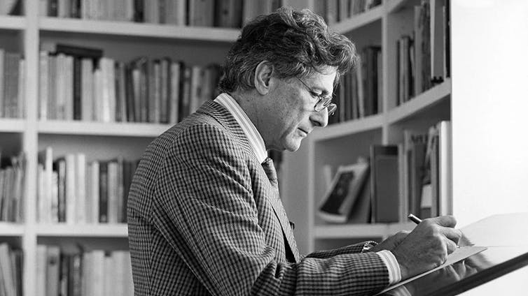 A man reads a book in front of bookshelves