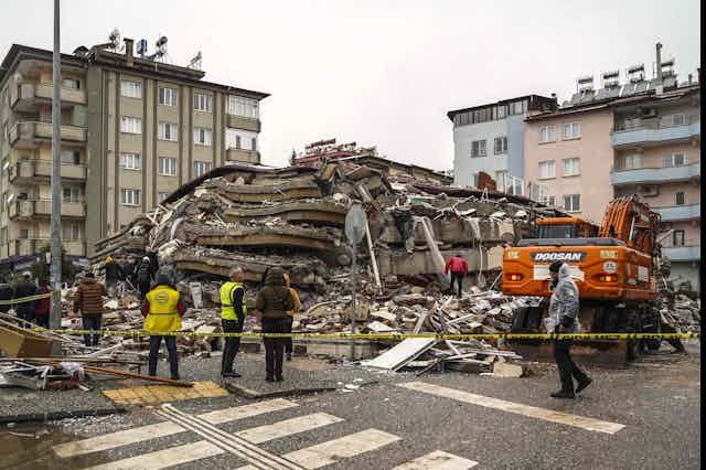 People stand in front of a collapsed building.