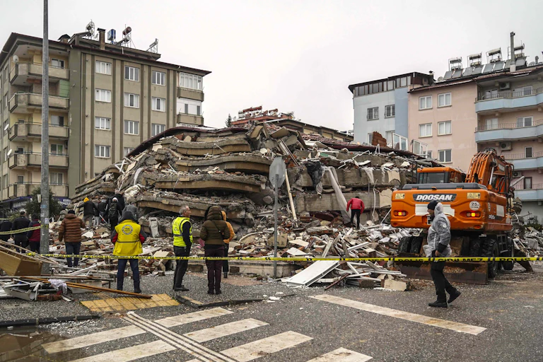People stand in front of a collapsed building.