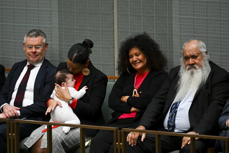 Four people sit in Parliament. Senator Jana Stewart is sitting with her baby, alongside Patrick Dodson and Malarndirri McCarthy.