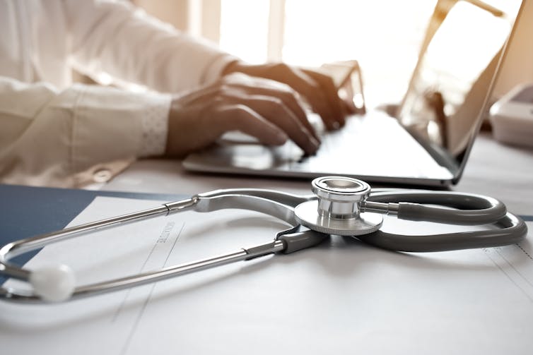 Doctor types on laptop next to a stethoscope