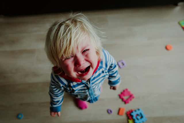 Vista cenital de un niño rubio vestido a rayas azules llorando desconsoladamente.