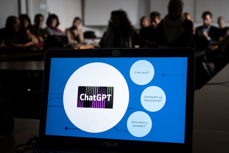 A screen displaying a ChatGPT logo stands at the front of a room packed with teachers