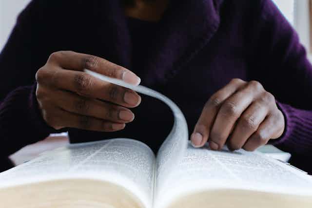 A person flipping through a Bible, with the right hand holding a page and a finger on the left hand pointing at a section of the book. The person's face is not in the picture