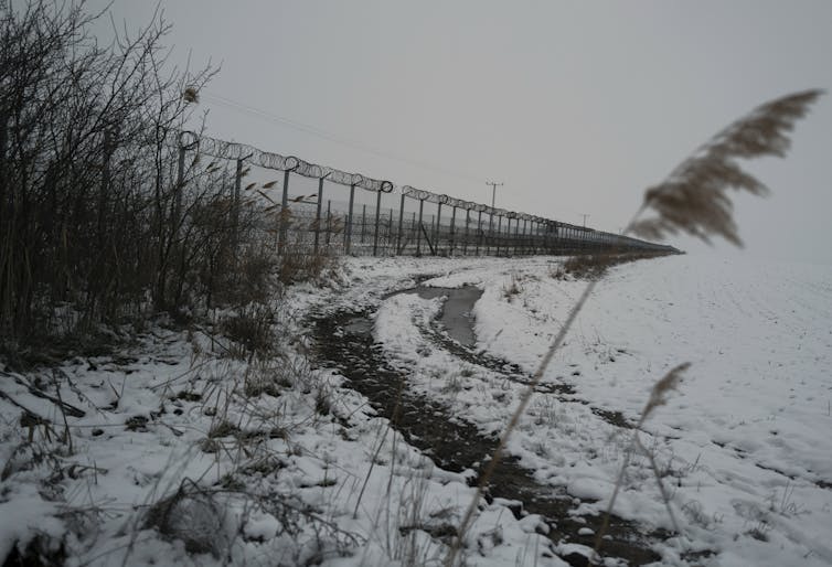 A long chain-link fence runs beside a snowy field.