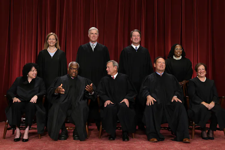 Five men and four women are wearing black robes as they pose for a portrait.