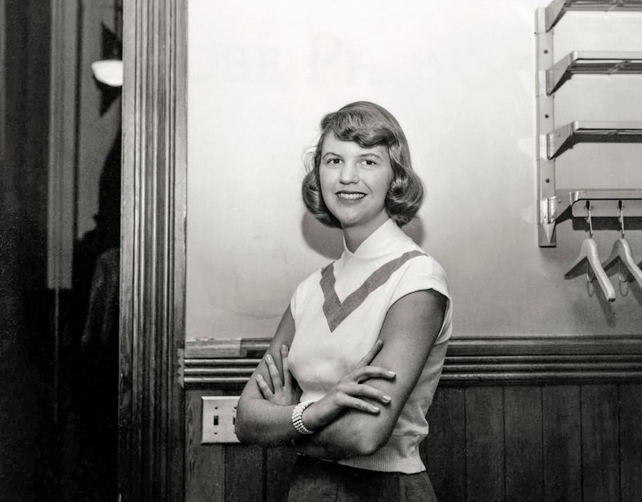 Sylvia Plath poses with her arms crossed, smiling.