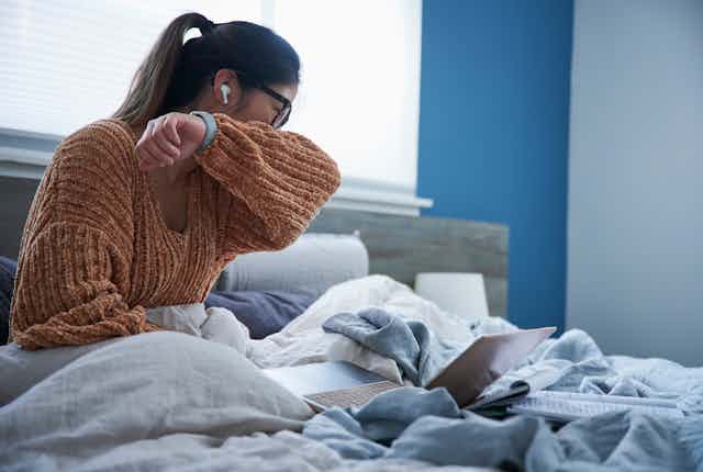 A woman coughing into her elbow while sitting in bed. 