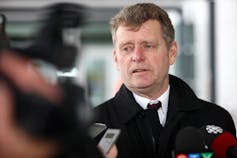 A man wearing a suit speaking into microphones.
