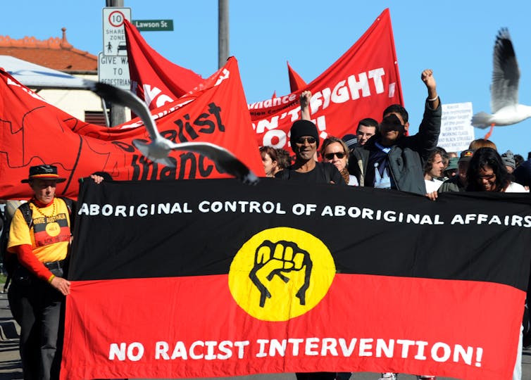 People are protesting while holding a sign that reads 'Aboriginal control of Aboriginal Affairs - No Racist Intervention'