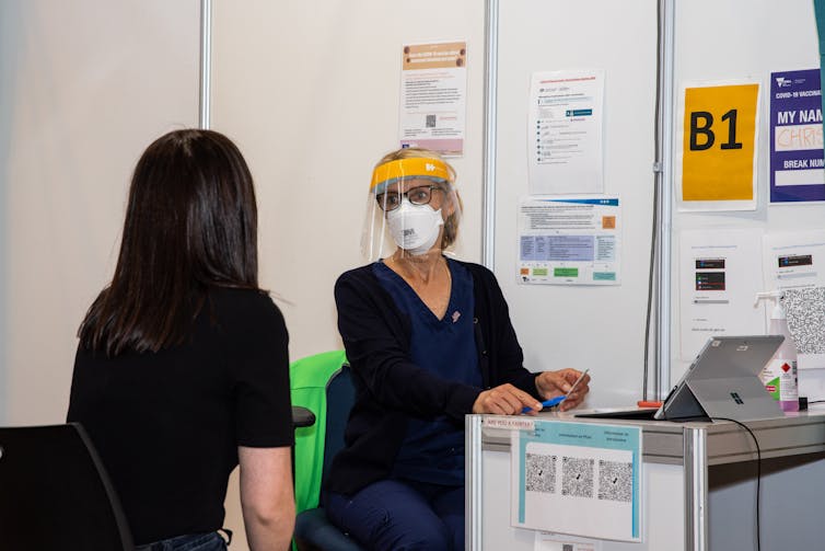 Nurse talks to vaccination patient in cubicle