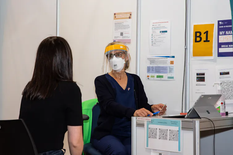 Nurse talks to vaccination patient in cubicle