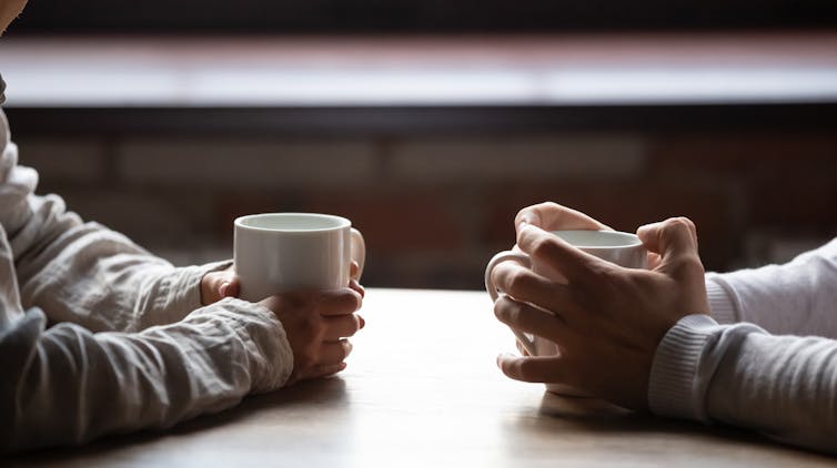 Close up woman and man sitting in cafe, holding warm cups of coffee on table