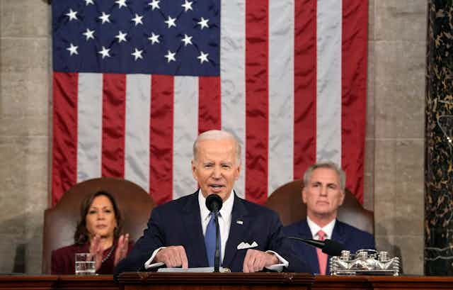 Joe Biden stands at a podium in front of vice-president Kamala Harris and House speaker Kevin McCarthy.