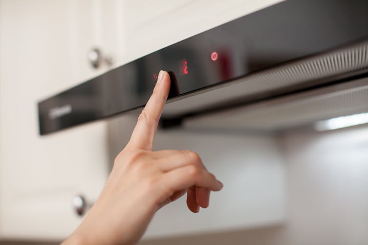 A hand presses a button on an extraction fan above an oven.
