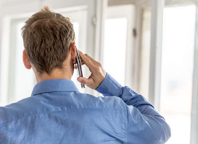 A man in a blue shirt seen from behind, talking on the phone