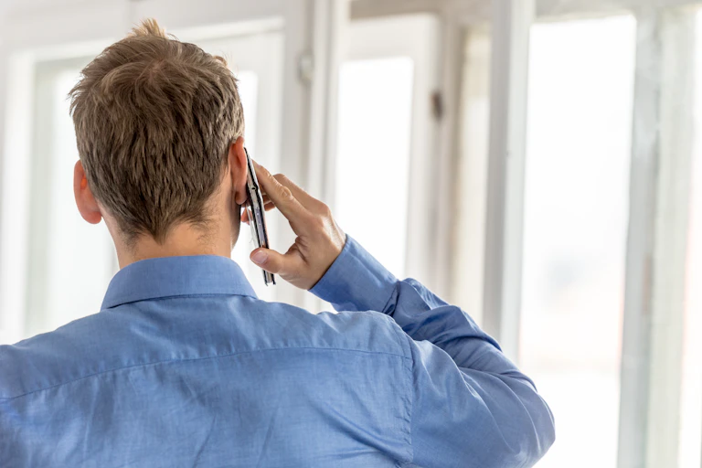 A man in a blue shirt seen from behind, talking on the phone