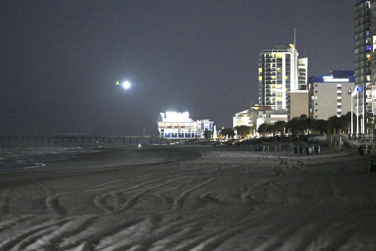 A dark photo shows a bright white circle over a dark beach, next to a lit up Ferris wheel and some buildings along the shore.
