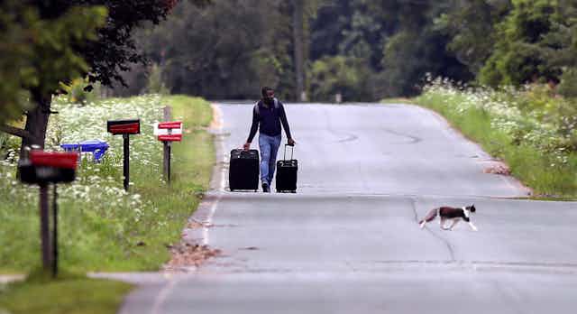 Un homme portant deux valises marche sur une route