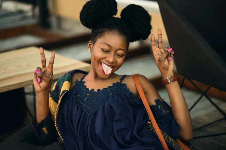 Woman smiling and doing peace signs with eyes closed.