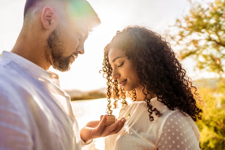 A man holds a ring box while proposing to a woman.