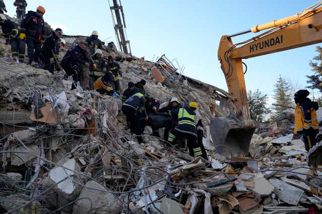A group of people wearing helmets and reflective jackets on the rubble of a collapsed concrete building