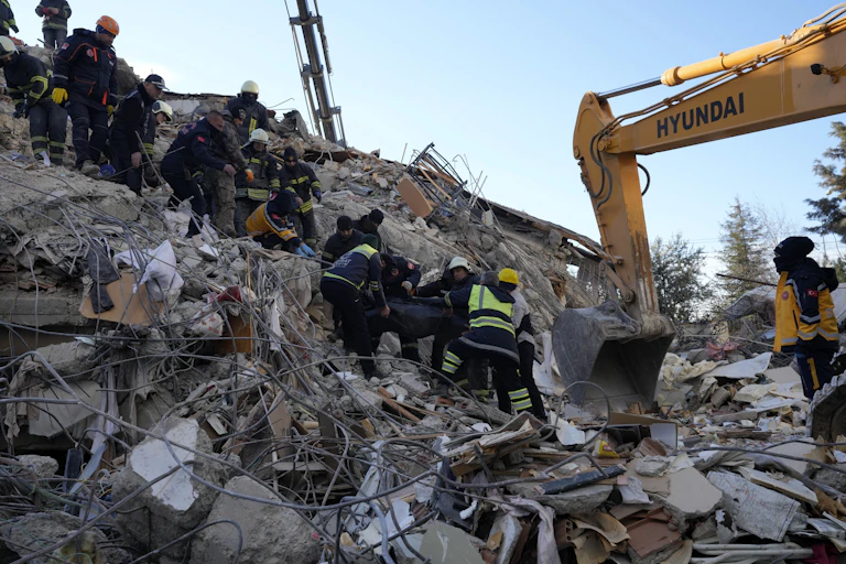 A group of people wearing helmets and reflective jackets on the rubble of a collapsed concrete building