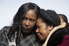 Two black women press their heads together.