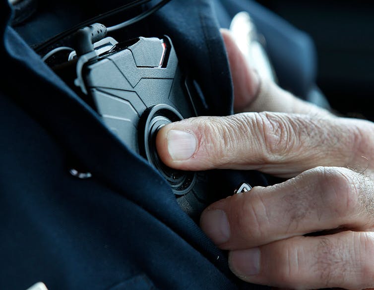 A man's finger pressing a button on a device placed on a blue police uniform.
