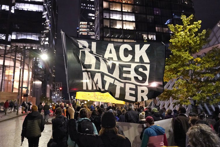 People carry a Black Lives Matter flag as they walk along a downtown street at night.