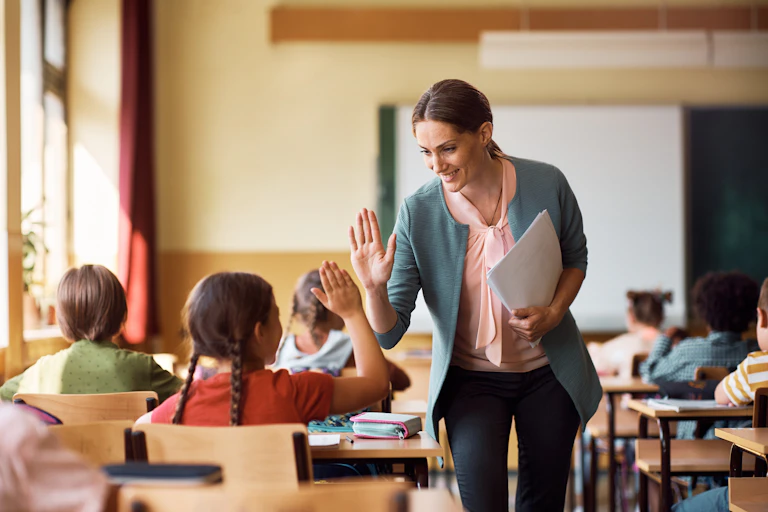Profesora y alumna en aula se chocan las palmas de la mano derecha.