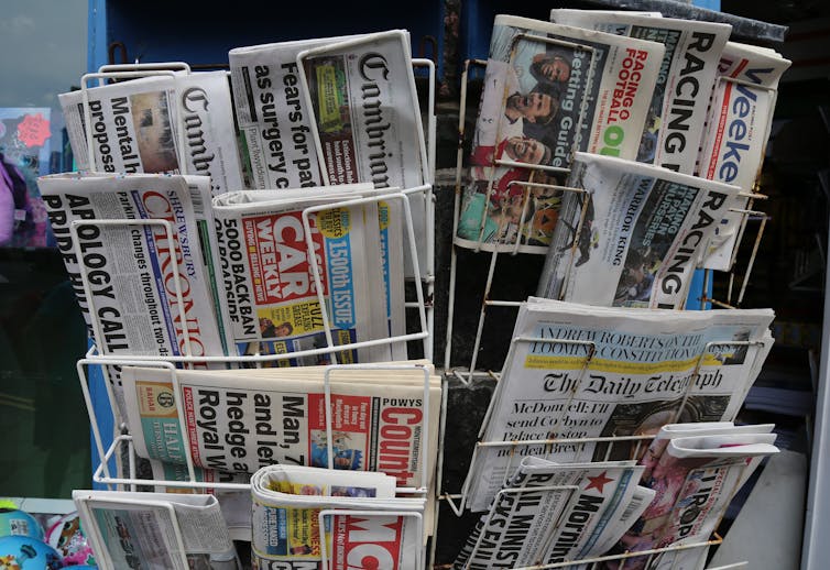 A selection of different newspaper brands are stacked in a display.