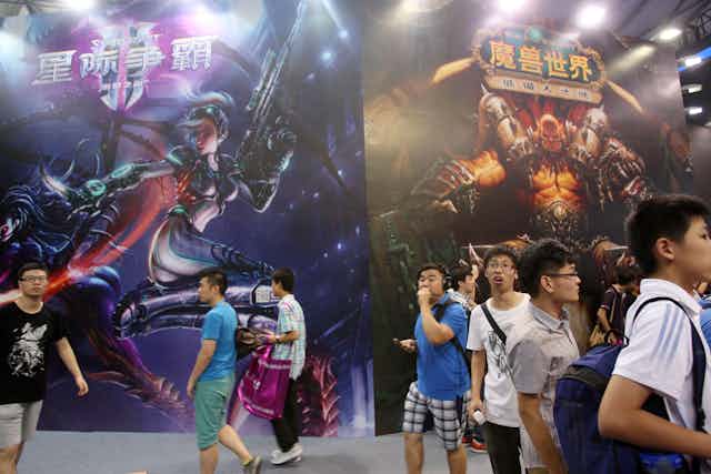 Young boys stand in front of large-scale posters for a video game.