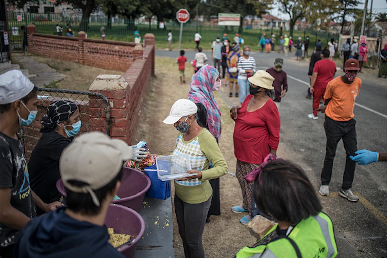 People wearing COVID masks queue for food parcels on a pavement.