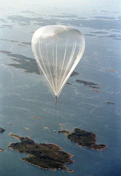A giant translucent weather balloon floats over open water and islands.