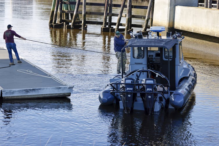 A man pulls a boat by a rope towards a dock.