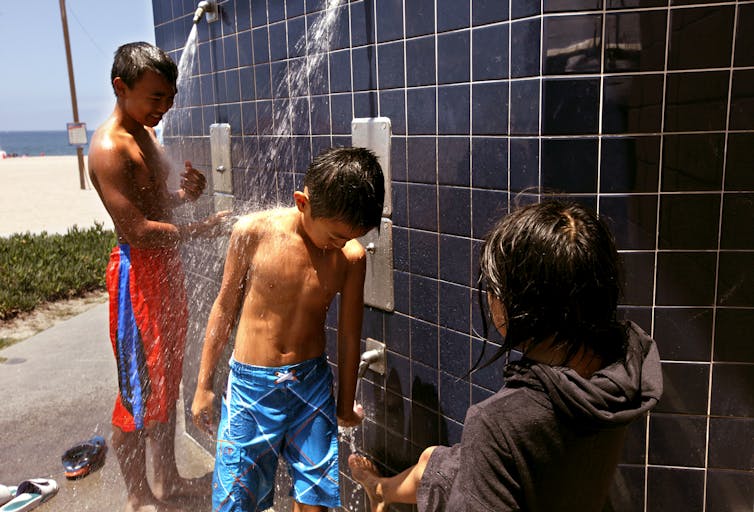 Children use an open-air shower at a public beach.