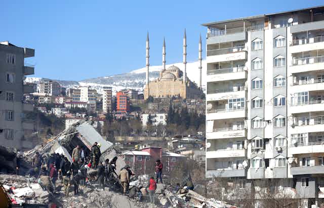 A group of rescue workers stands on a pile of rubble from a collapsed building after the Turkey earthquake, February 2023.