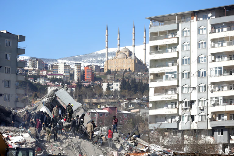 A group of rescue workers stands on a pile of rubble from a collapsed building after the Turkey earthquake, February 2023.