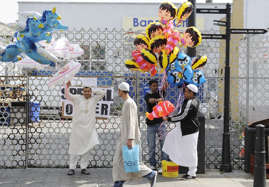 Three men hold large bunches of colourful balloons while another man walks past