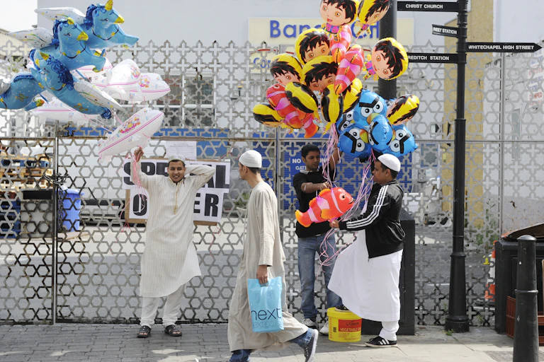 Three men hold large bunches of colourful balloons while another man walks past
