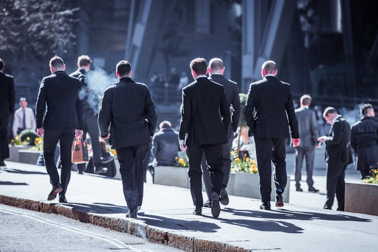 Four white men in suits walking away from the camera