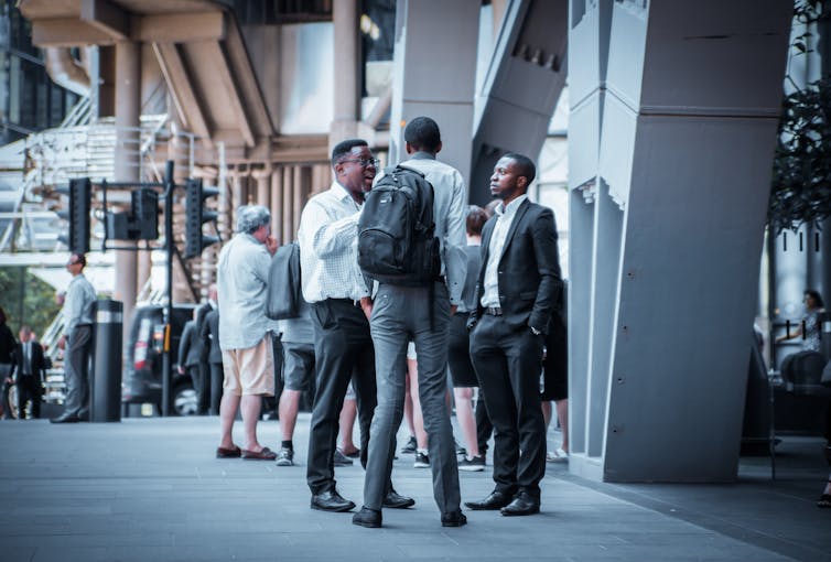 Three Black men in suits chatting outside an office building