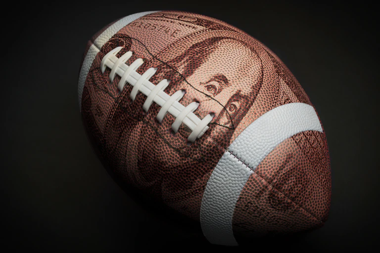 A graphic of a football with a one hundred dollar bill superimposed over it.