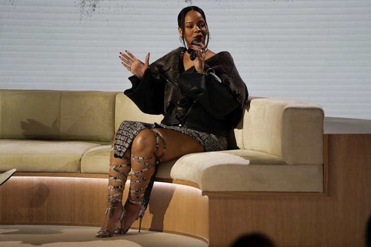 Signer Rihanna in a black outfit sitting on a couch speaking into a microphone.