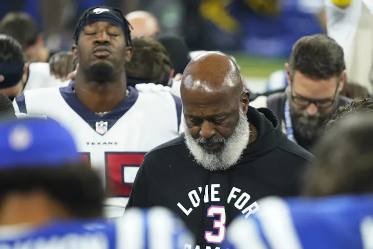 People stand, head bowed, eyes closed.