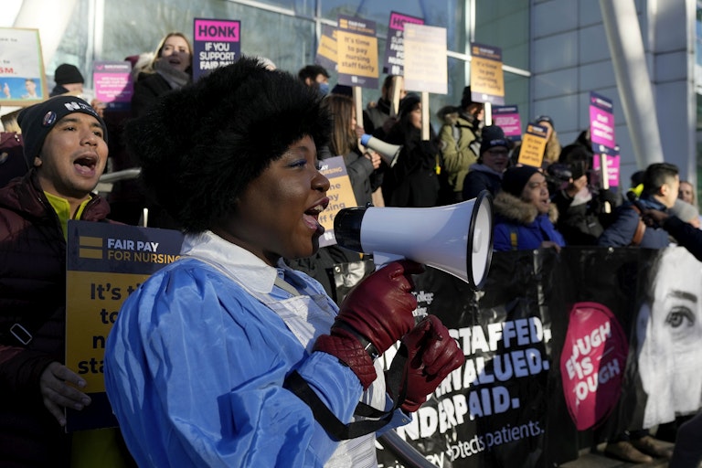 A woman speaking into a megaphone in front of protesters holding placards